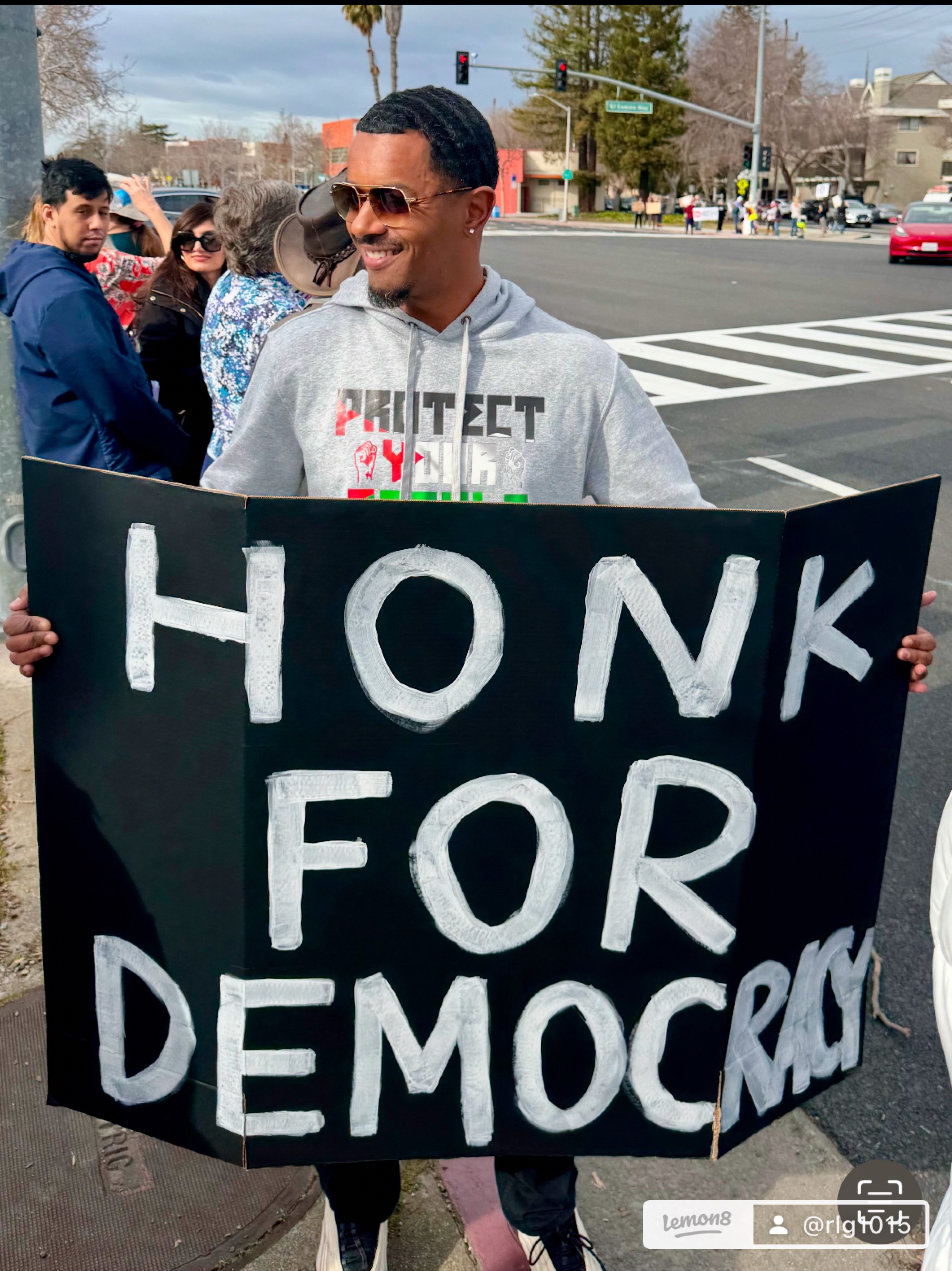 Raymond Goins holding a handmade sign reading Honk for Democracy at a Palo Alto street corner
