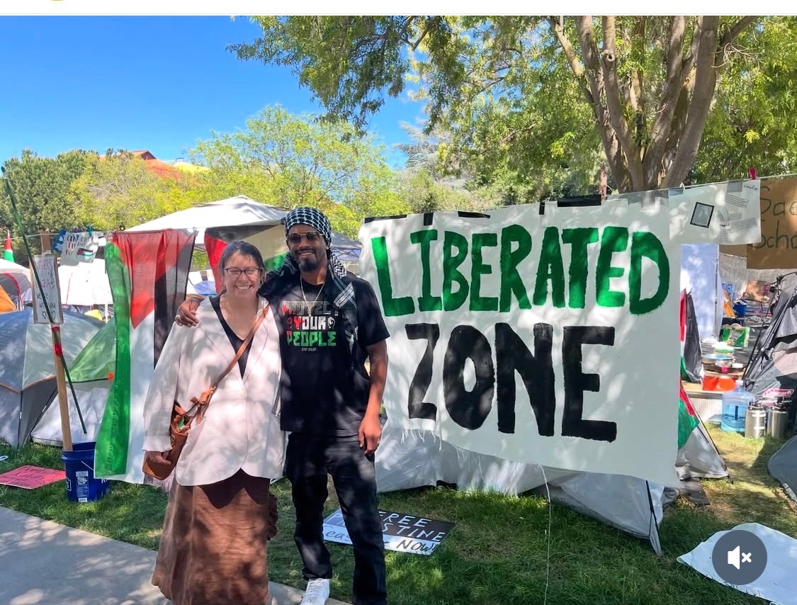 Raymond Goins standing with a fellow organizer in front of a Liberated Zone banner at a community encampment